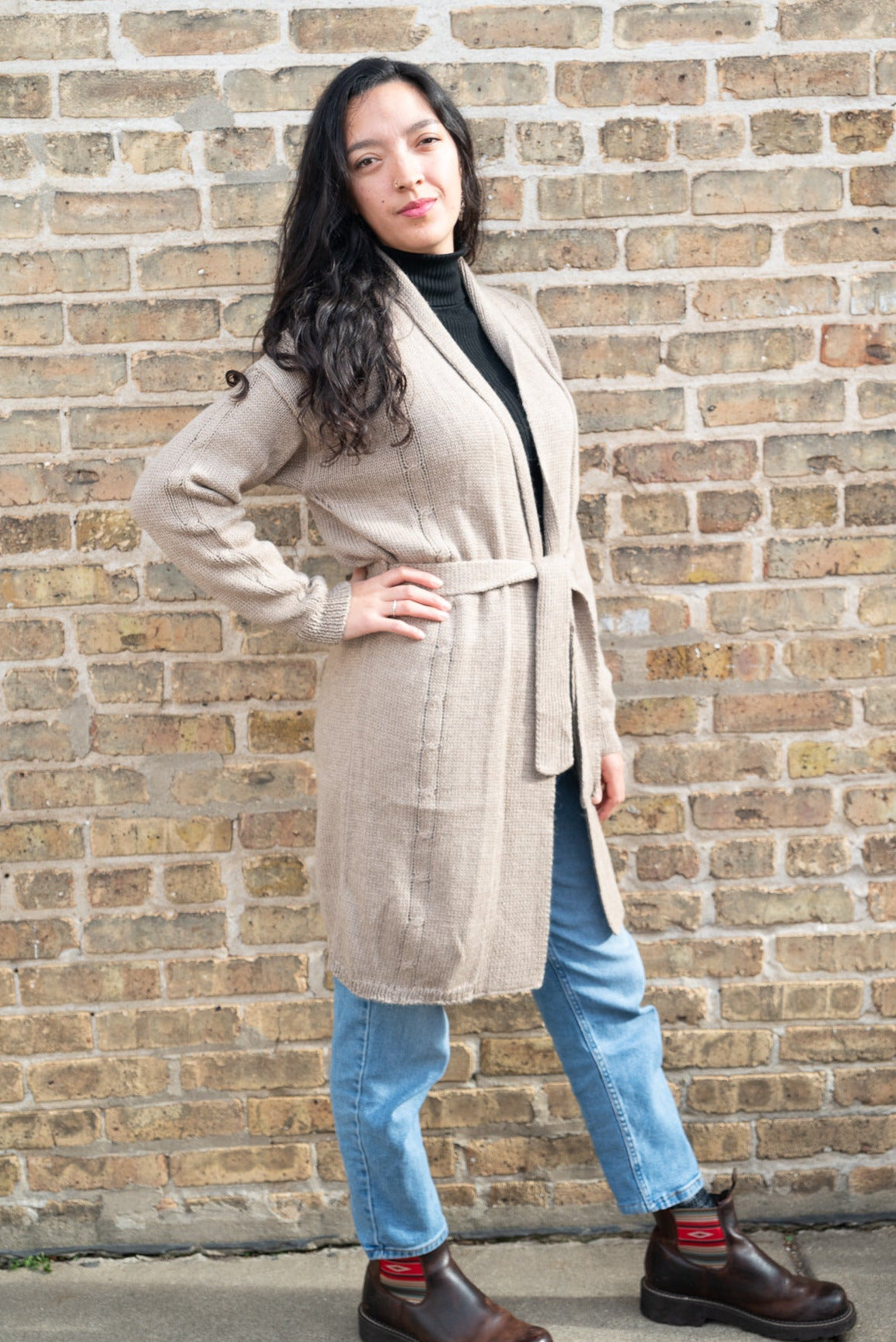 Woman wearing a beige coat standing against a brick wall