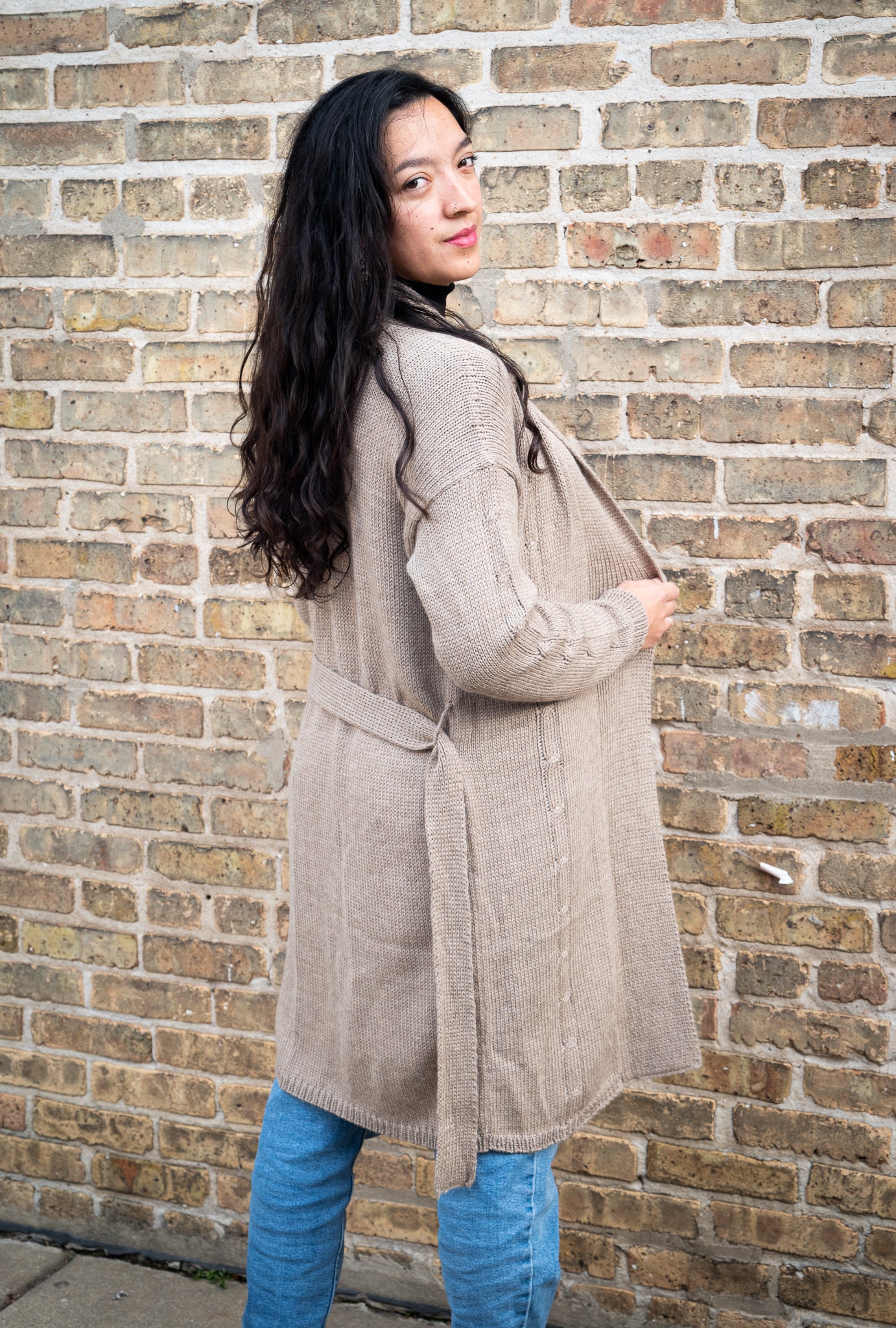Woman wearing a beige coat standing against a brick wall