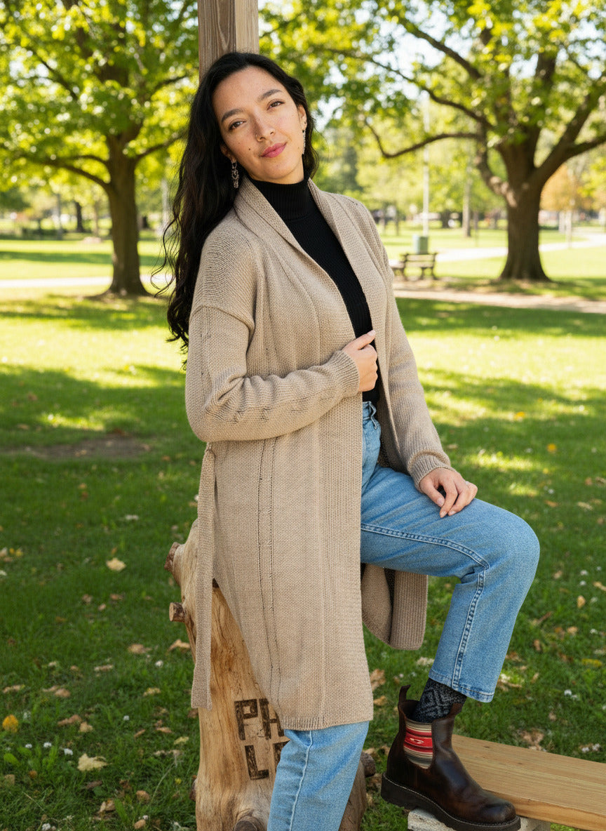 Woman wearing a beige cardigan, black shirt, blue jeans, and brown boots. 