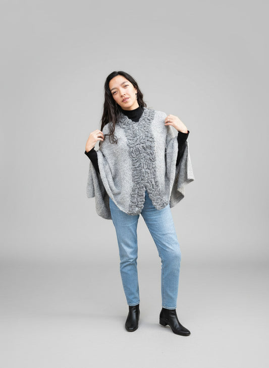 Woman wearing a gray poncho against a brick wall