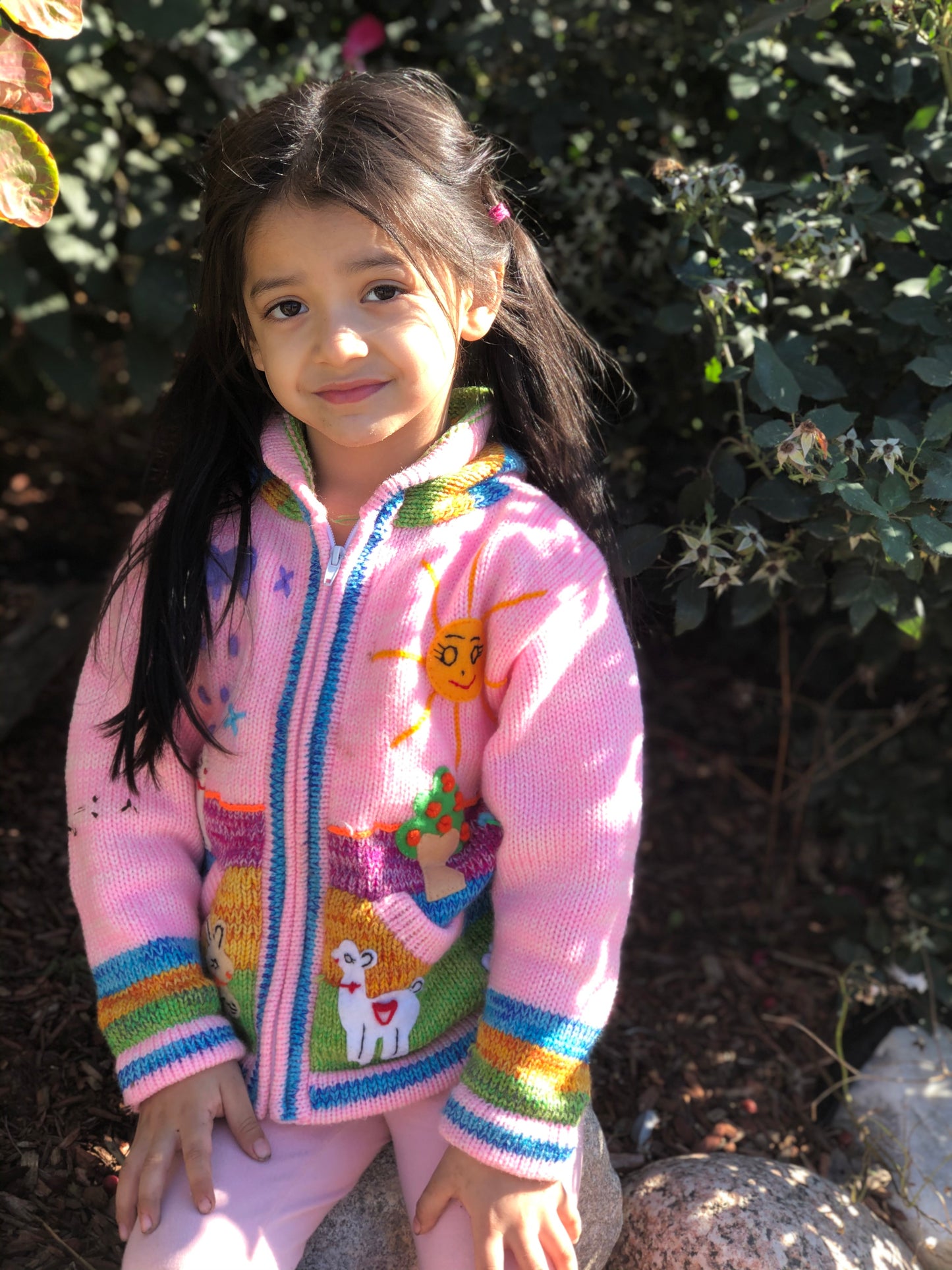 Young girl wearing a pink alpaca kids sweater with llama, sun and tree designs