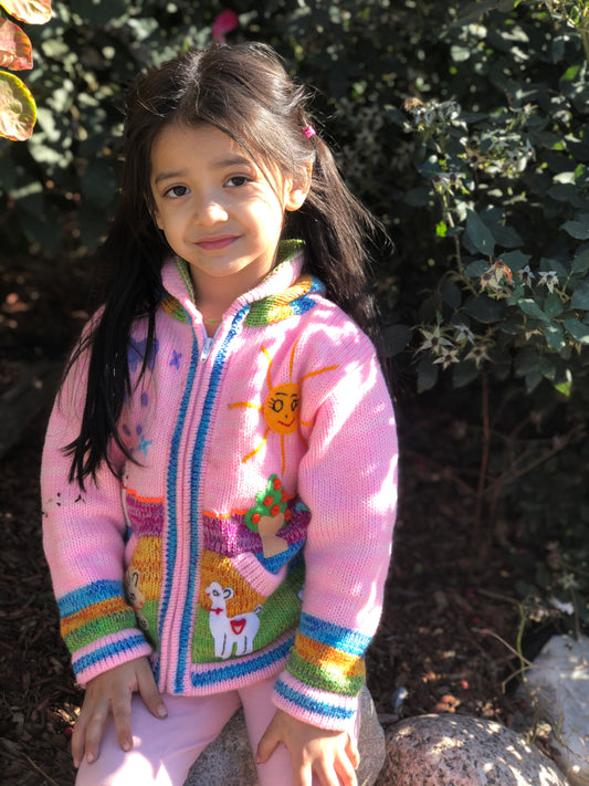 Young girl wearing a pink alpaca kids sweater with llama, sun and tree designs
